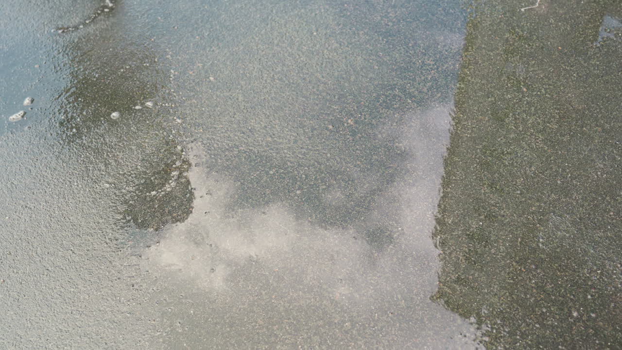 puddle reflection cloudy sky wet asphalt. Slow raindrops create delicate ripples across shimmering surface, scattered droplets and textured pavement capture moody urban atmosphere, overcast light