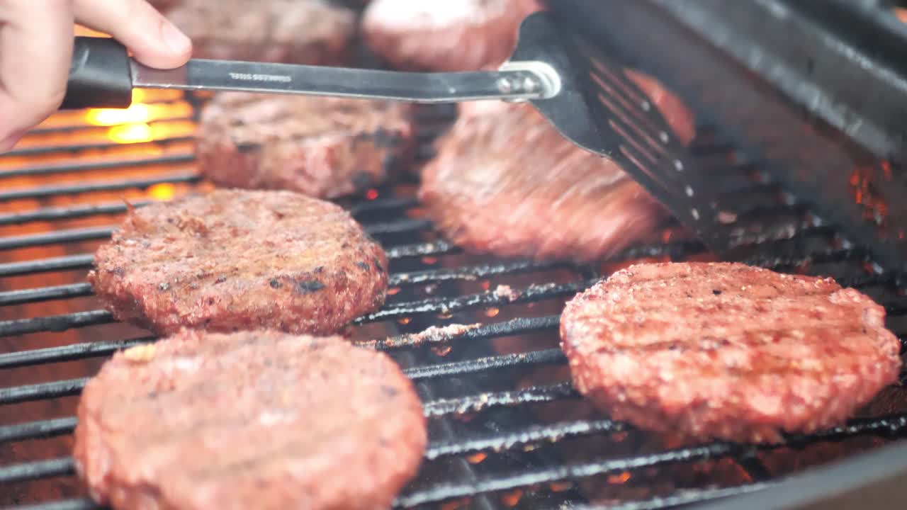 Coperchio che si apre sul grill e spatola che gira hamburger vegetali su un barbecue, inquadratura ampia in panning con fiamma al rallentatore 4K.
