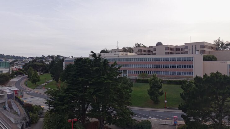 Panoramica aerea rivelatrice degli edifici del campus del City College di San Francisco e del paesaggio circostante, che mostra l'architettura accademica e l'ambiente da parco urbano in una giornata nuvolosa in California.