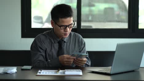 successful cheering asian men counting money celebrating victory with a lot of money. young asian businessman counting dollars on the table in room