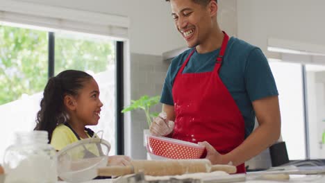 Happy-biracial-father-and-daughter-baking-together-in-kitchen