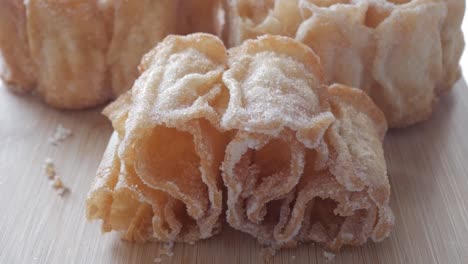zoom out reveals a golden spanish sweet, flor frita, resting on a wooden board dusted with sugar