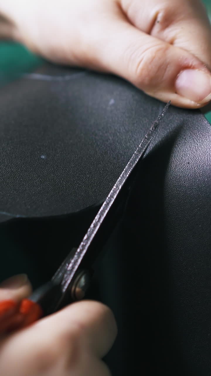 CU: Workshop master cuts black leather fabric with large special scissors against green cutting board closeup