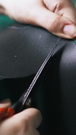 cu: workshop master cuts black leather fabric with large special scissors against green cutting board closeup