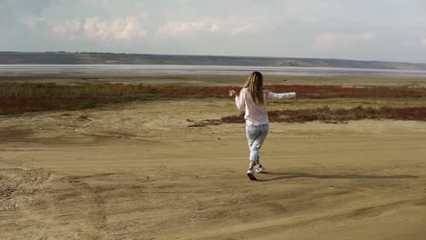 Young-woman-is-dancing-alone-standing-on-sand-beach-with-lake-line-on-background