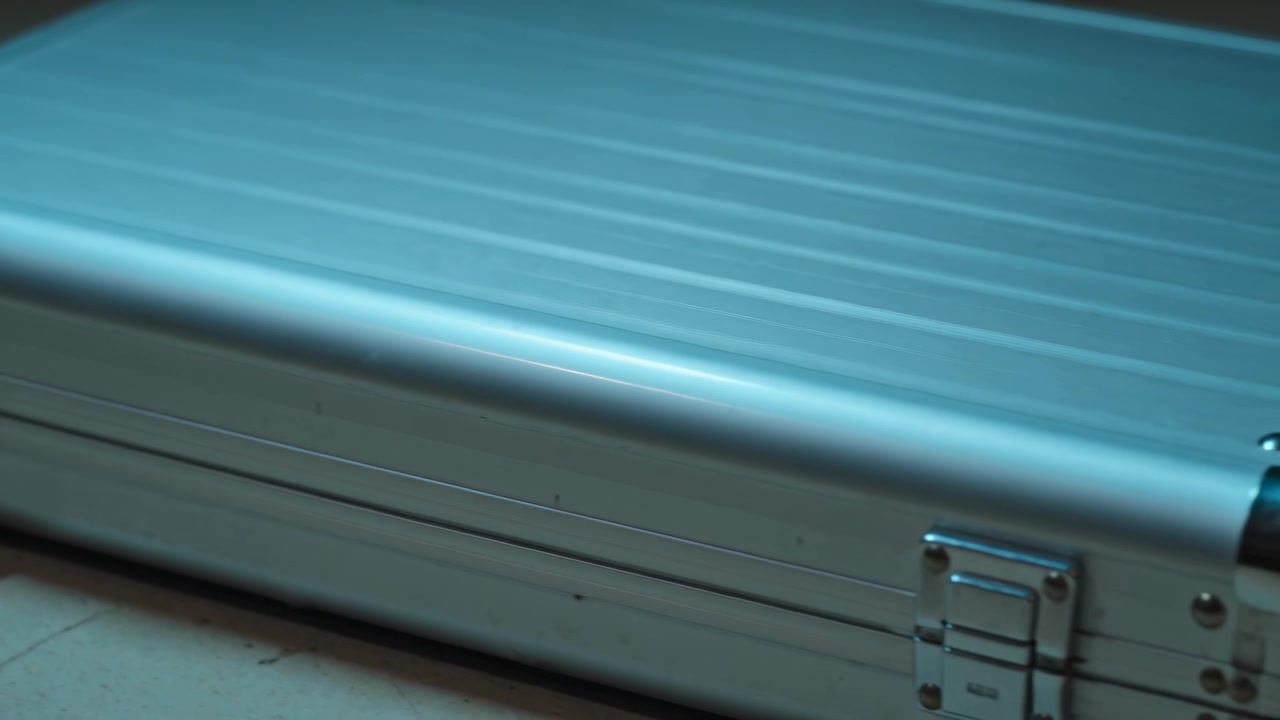 Panning camera revealing silver aluminum briefcase on light floor, to showcase latches and handle