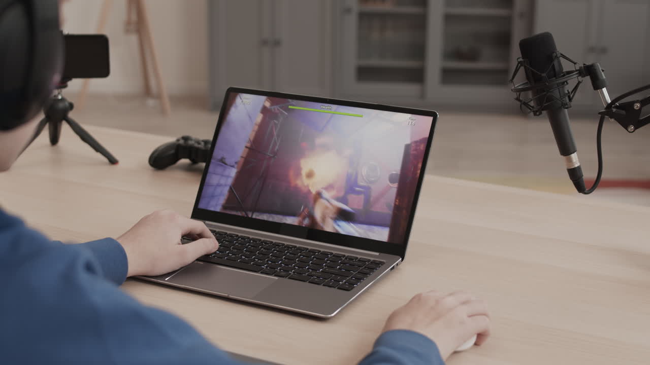 Gamer playing a video game on a laptop with microphone and headphones