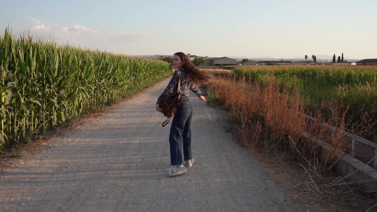 Una joven camina alegremente por un pintoresco sendero rural rodeada de exuberante vegetación.