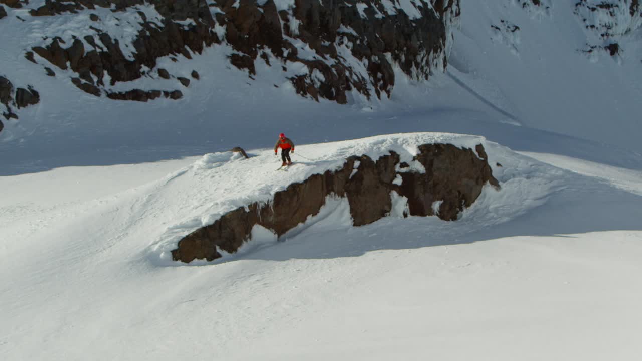 esquiador con chaqueta roja dando un salto de fe desde un acantilado rocoso, deporte extremo