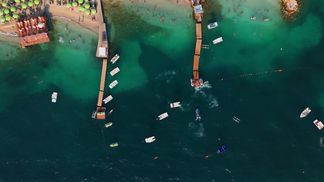 Tourists swimming near wooden piers and boats in the clear turquoise waters of ksamil, aerial view