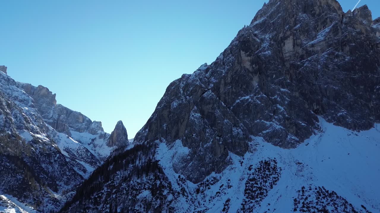 Drone che sorvola il silenzio alpino, rivelando le Dolomiti innevate sotto un cielo blu intenso