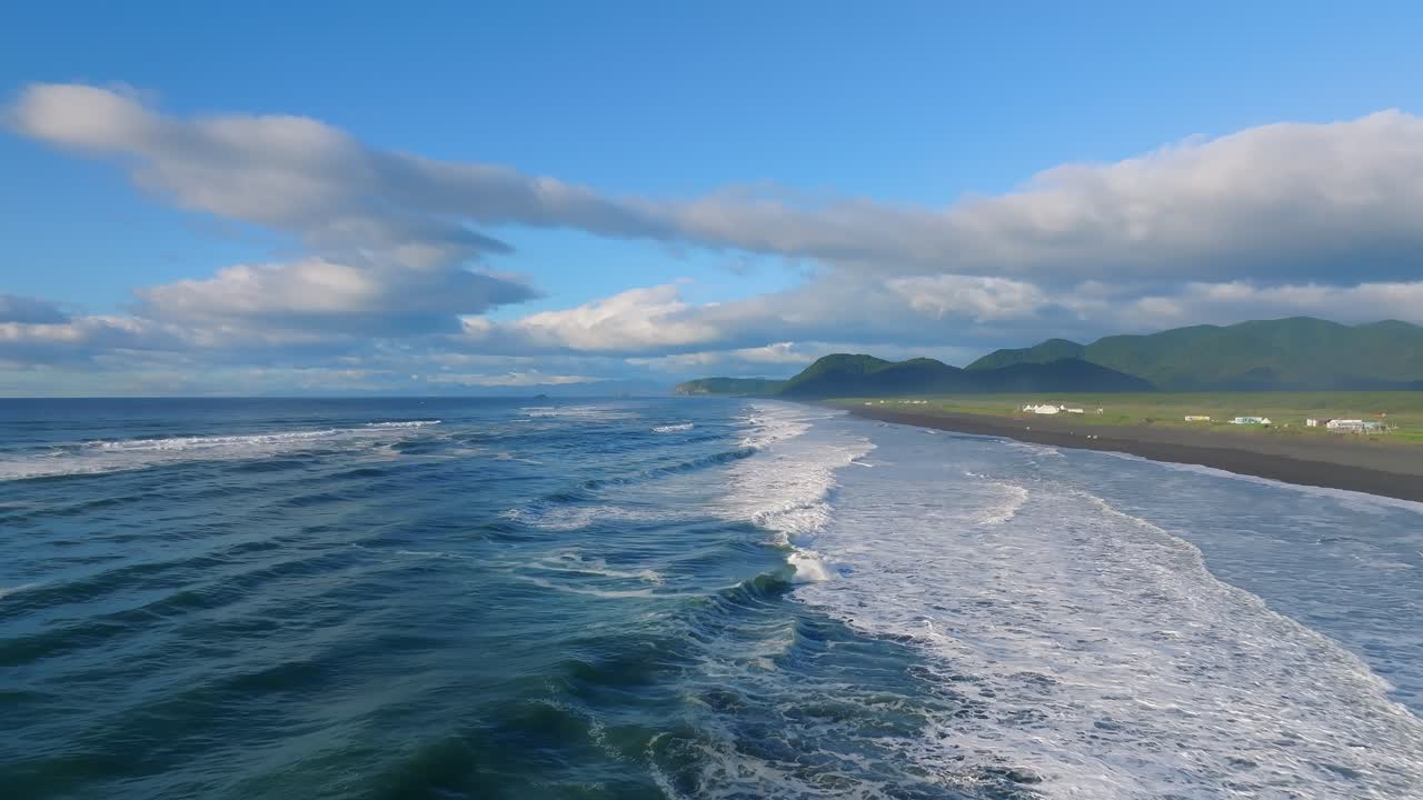 Veduta con drone delle onde che si infrangono sulla costa di sabbia nera della Spiaggia di Khalaktyrsky, Territorio della Kamchatka, Russia, con montagne, nuvole e il vasto Oceano Pacifico.