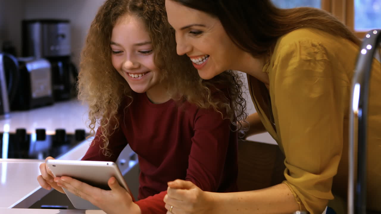 Daughter and mother are looking a tablet on a bed 