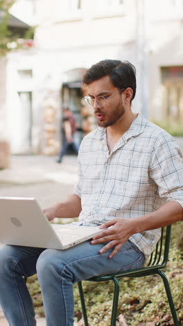 indian young man freelancer sitting on chair opens laptop start working online distant job outdoors