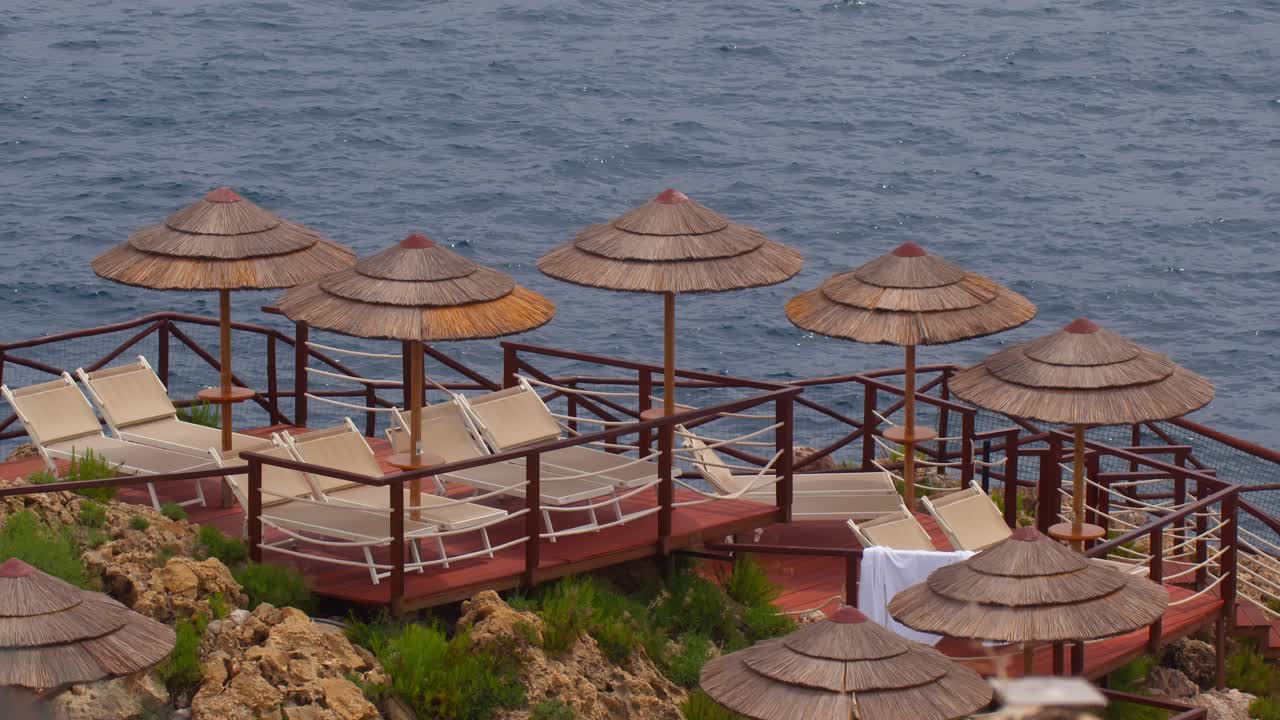 Straw parasols and chairs on deck with sea and waves in Taormina, Sicily, Italy (Italia)