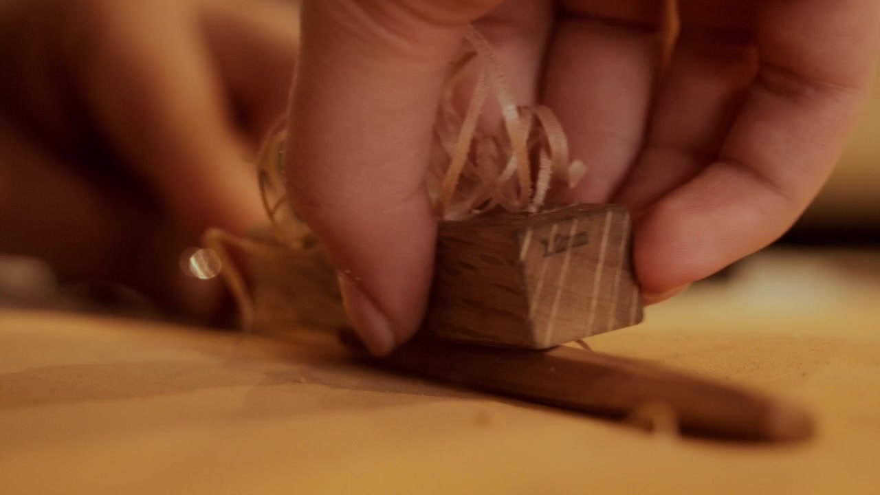 Manos de artesano cepillando cuidadosamente una superficie de madera con un pequeño cepillo de mano.