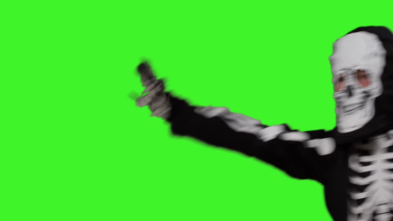 Child Dressed Up In Skeleton Costume Trick Or Treating At Halloween Moving Across Frame Against Studio Green Screen