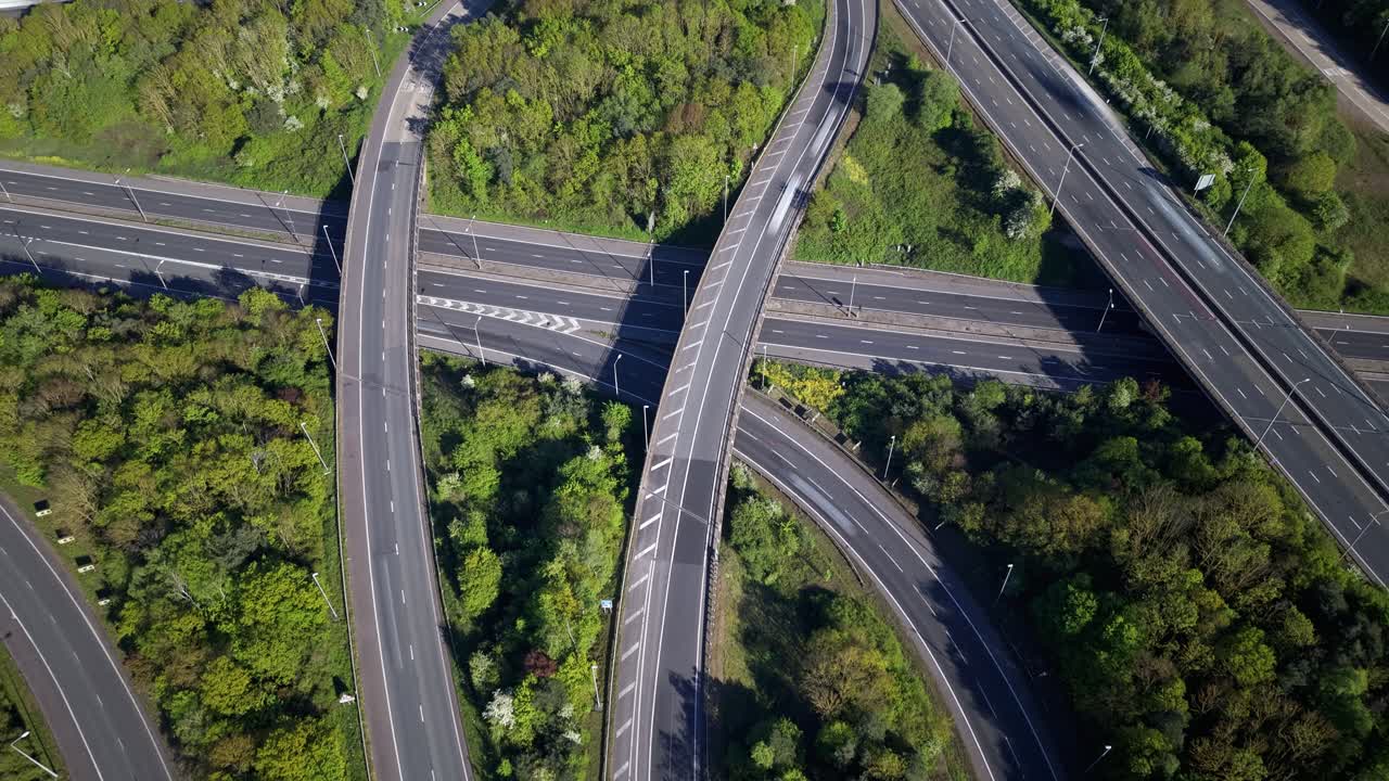 Aerial timelapse of a major UK motorway junction during daytime. Vehicles move swiftly through the complex road network. This hyperlapse shows the continuous flow of busy traffic at the interchange