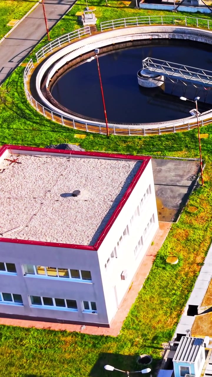 Ovenfra udsigt over renseanlægsbygning. Hvid tagkonstruktion ved siden af cirkulær klareringstank med blå vinduer og grøn plæne. Vertikal video