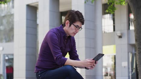 Asiatischer-Mann-Nutzt-Digitales-Tablet,-Während-Er-In-Der-Nähe-Des-Unternehmensparks-Sitzt