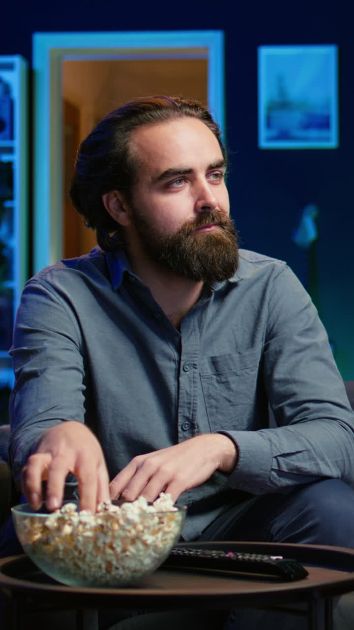 Vertical video Man at home on couch gripped by interesting film shown on television screen