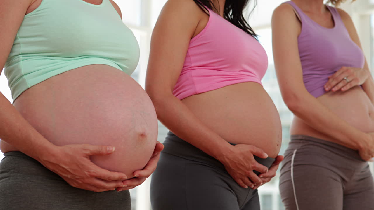 Fitness stüdyosunda ayakta duran ve karınlarını tutan hamile kadınlar.