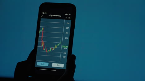 on the screen of a mobile phone the broker watches the chart changes and shows the growth and fall of shares against the background of a changing table