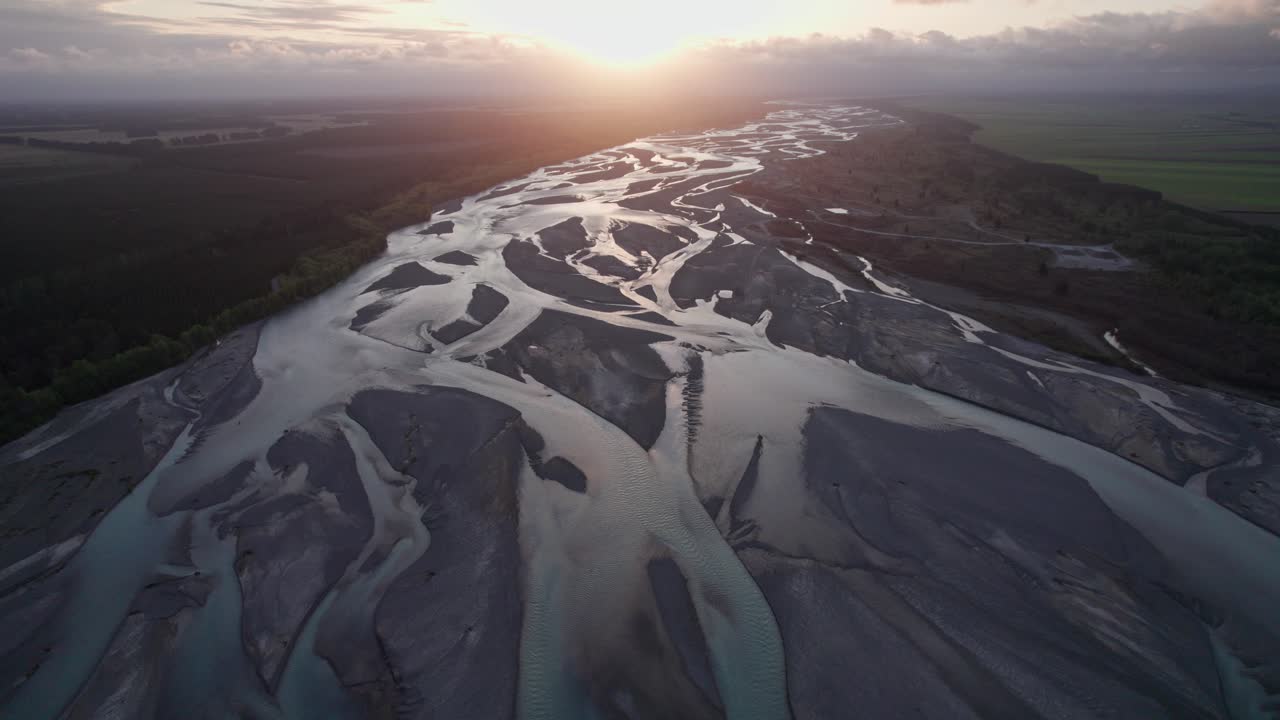 vuelo aéreo hacia atrás sobre el río trenzado waimakariri con la puesta de sol proporcionando luz dorada en los canales, christchurch, nueva zelanda