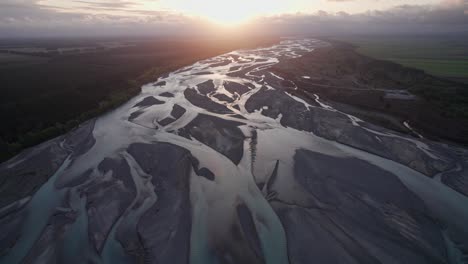 Vuelo-Aéreo-Hacia-Atrás-Sobre-El-Río-Trenzado-Waimakariri-Con-La-Puesta-De-Sol-Proporcionando-Luz-Dorada-En-Los-Canales,-Christchurch,-Nueva-Zelanda