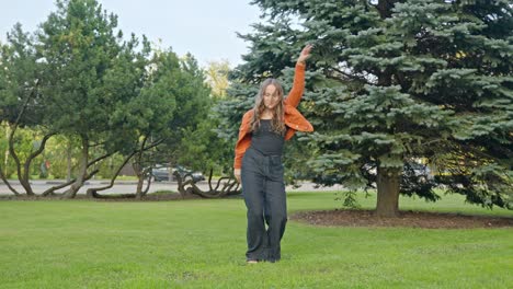 Woman-dancing-freestyle-by-herself-on-green-grass-in-park,-enjoying-moment