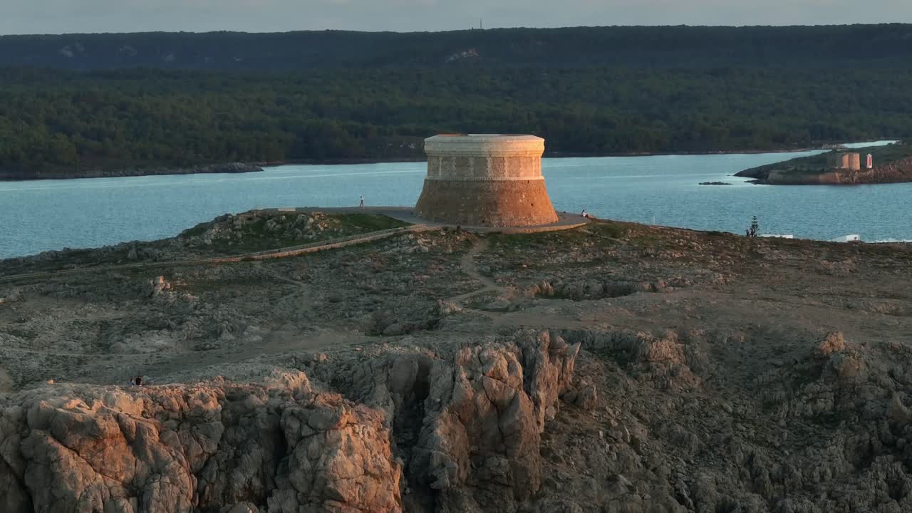 беспилотник пролетает над оборонительной башней на менорке в испании, чтобы показать маленький городок форнеллс на закате солнца