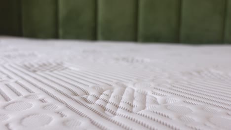 closeup of a white quilted mattress with a green headboard in the background