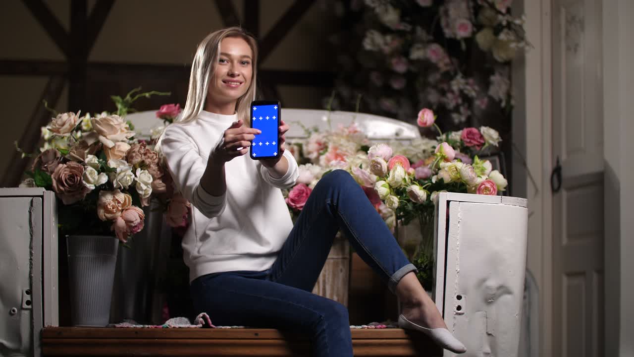 Portrait of lean smiling girl with blue chromakey screen smartphone in hands.
