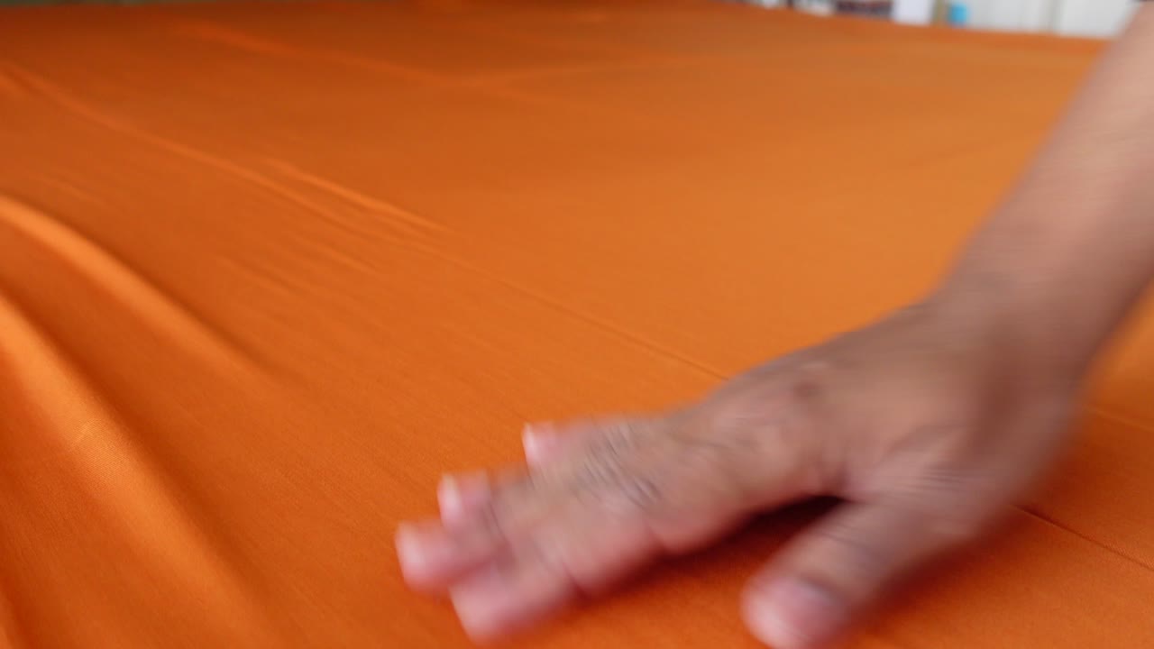 Die Hand einer Person glättet ein großes Stück orangefarbenen Stoff