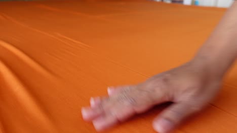 die hand einer person glättet ein großes stück orangefarbenes gewebe aus