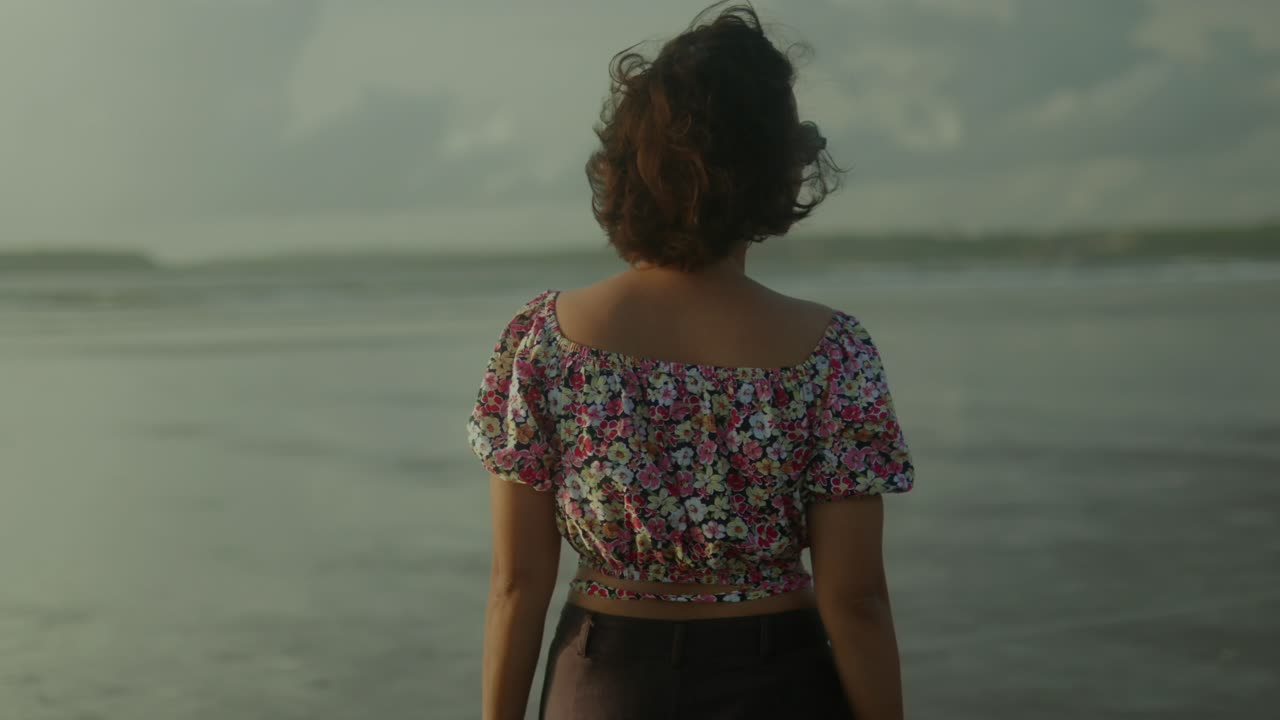 Back View of a beautiful carefree young girl slowly walking on a sea coast
