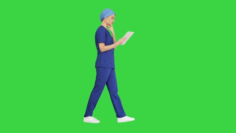 young woman doctor or nurse in scrubs using a touchscreen computer while walking on a green screen, chroma key