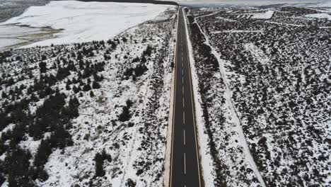 Long-empty-road-aerial-into-distance-across-highland-snowy-countryside-moors-tilt-down-birdseye