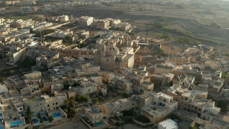 Kirche-Mitten-In-Einer-Kleinen-Mediterranen-Stadt-In-Beige-Und-Brauner-Sandfarbe-Auf-Der-Insel-Malta,-Luftdrohnenperspektive,-Dolly-Nach-Vorne