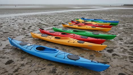 a colorful array of kayaks resting on a sandy shoreline as a figure walks along the tidal flats, capturing the tranquility of nature and water sports