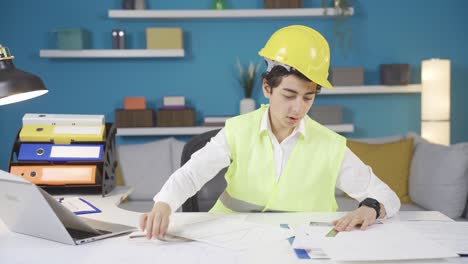 curious boy in yellow vest and helmet sitting at table at home, dreaming of being an engineer.