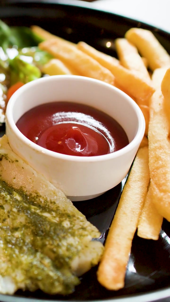 Primo piano di pesce alla griglia con pesto, patatine fritte e insalata che viene tagliato con una forchetta