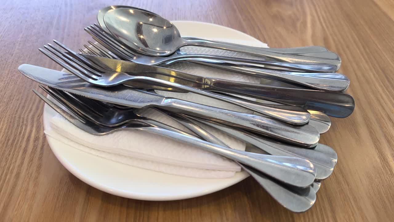 Clean silverware rests neatly on a white plate and napkin. The cutlery is set on a dining table. Everything is ready for the upcoming meal service