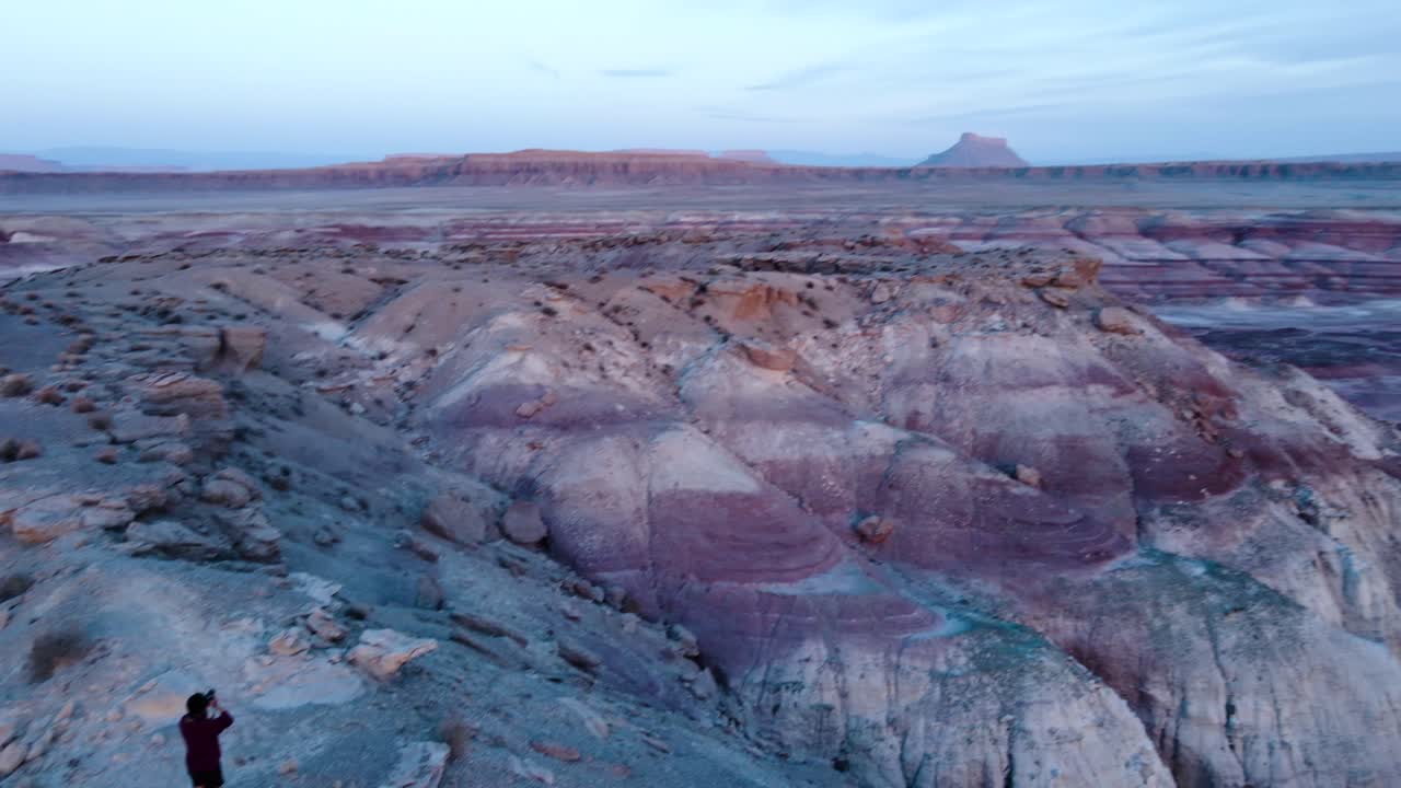 hiker and shorts and a red T-shirt walking over a mountain spine the landscape of red and blue rocks at blue hour in bentonite hills utah hanksville
