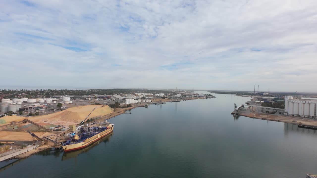 slow flight tover the port adelaide dockyard showing a ship in the foreground with cars and winding waterway in to the sea