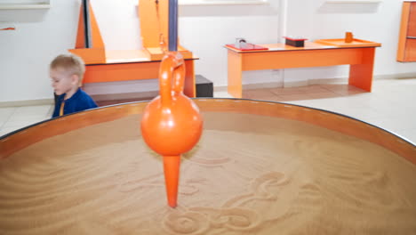a little boy visiting a science museum for children. he plays with a sand pendulum
