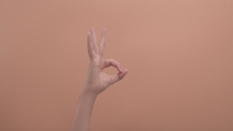 close-up of a woman's hand makes a shape that means ok with colored background