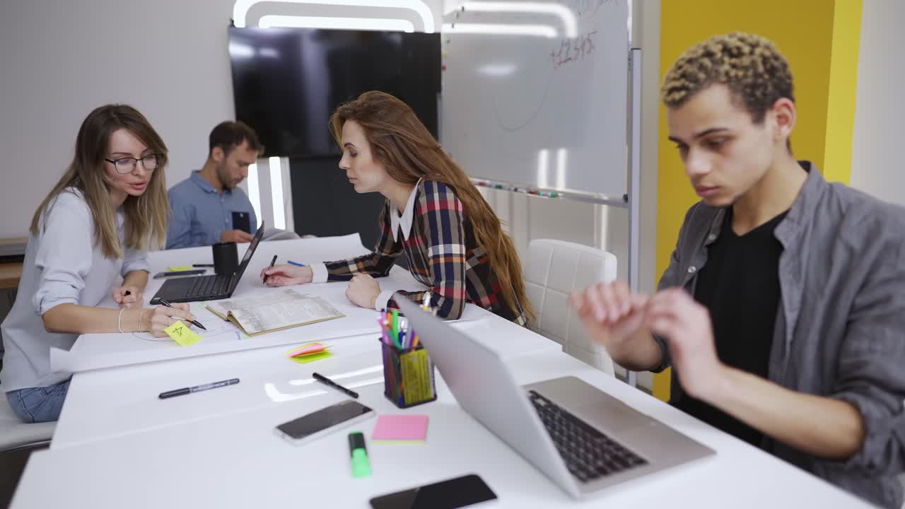 Unge kreative forretningsfolk kommunikerer og arbejder med laptops på kontoret