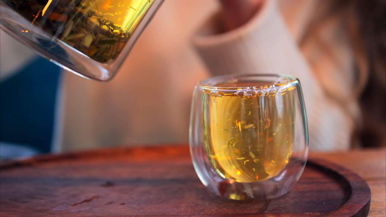 Close up of a woman pouring tea from a French press into a double glass cup at a restaurant