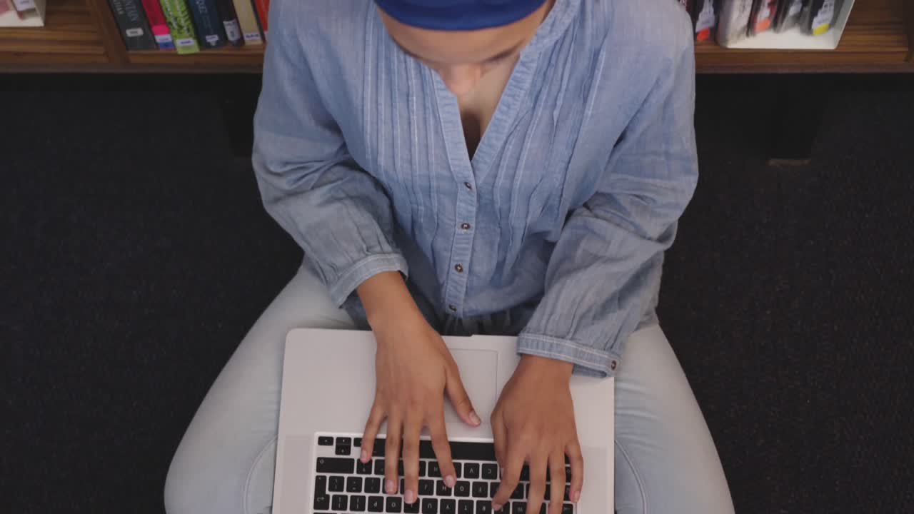 Asian female student wearing a blue hijab sitting on the floor and using a laptop